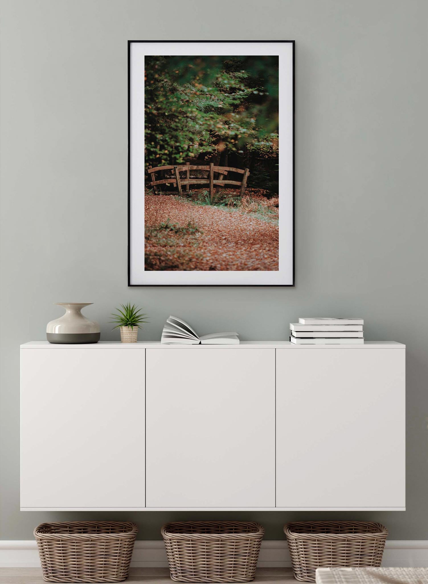 Woodland Bridge is a minimalist photography by Opposite Wall of a path covered in red leaves leading to a short and small arched bridge in the forest.